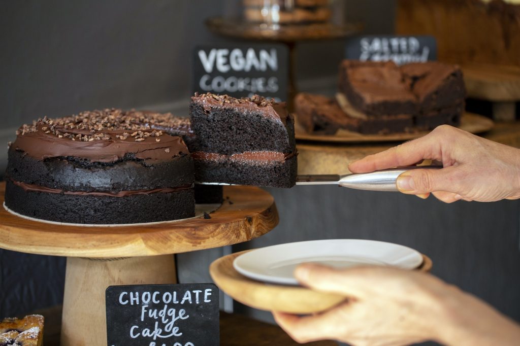 Close up of waitress putting slice of chocolate fudge cake on a plate door of a cafe.